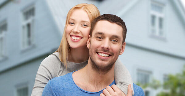 love, people, real estate, home and family concept - smiling couple hugging over house background
